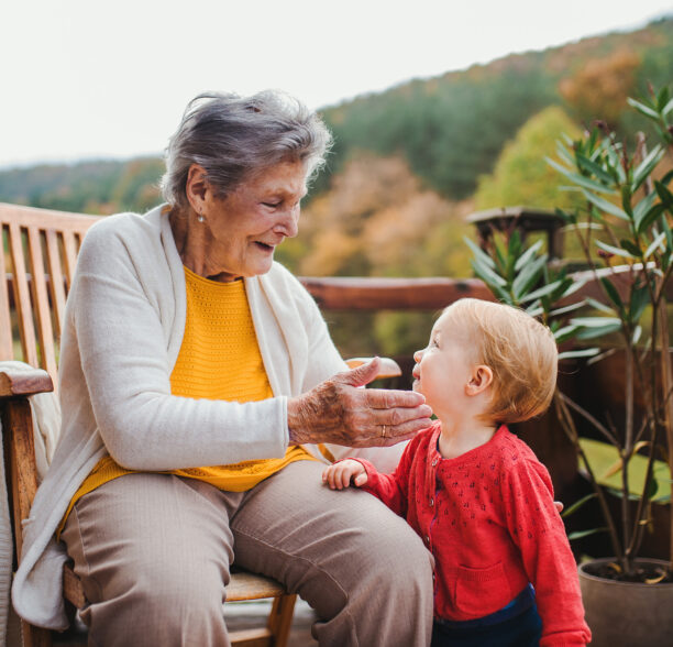 eine alte Frau sitzt auf einem Stuhl auf ihrem Balkon und spielt mit ihrem Enkel